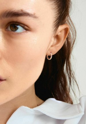 Huggie rõngad tekstureeritud hõbedasest viimistlusega, kaunistatud värviliste gemmidega. Suumi vaatamine, mis tõstatab rõngad naha vastu.