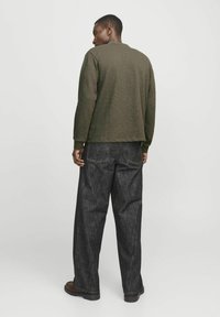 Suéter texturizado verde oliva de mangas largas, combinado con pantalones de mezclilla oscuros y de pierna ancha. Detalles de costura visibles y diseño de color sólido.