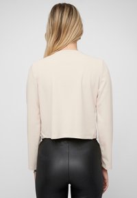 Světle růžový dlouhý rukáv cropped top vyrobený z měkké tkaniny, s kulatým výstřihem a jednoduchými, čistými liniemi. V kombinaci s černými legínami.