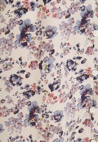 Květinová látka s modrými, růžovými a zelenými vzory na světlém pozadí. Obsahuje malé bílé knoflíky a má hladkou, jemnou texturu.
