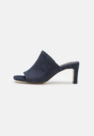 Mules de denim de tacón en un azul marino oscuro. Diseño de punta abierta con una textura suave y un frente ligeramente puntiagudo. Presentan un tacón delgado y elegante.