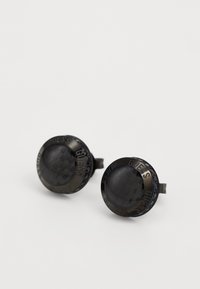 Boucles d'oreilles rondes noires avec une surface texturée, présentant un logo "GUESS" en relief sur le bord. Fabriquées en métal avec des accents brillants.