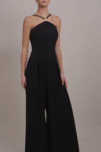 Tuta nera con corpetto aderente, scollatura a halter e pantaloni larghi plissettati. Presenta un'accente a diamante sulla scollatura.