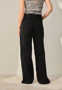 Vidbenede sorte denimbukser med baglommer, der har høj talje og en diskret struktur, kombineret med en mønstret top.