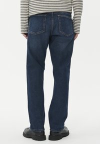 Temno modri kavbojke z ravnim krojem, obležane s dvema zadnjima žepoma in šivi; oblečene z črnimi veznimi škornji.