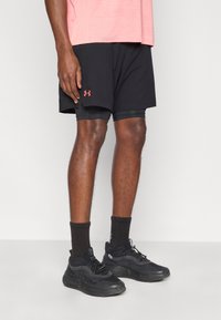 Μαύρο αθλητικό σορτς με εσωτερική επένδυση, διακοσμημένο με κόκκινο λογότυπο. Συνδυάζεται με μαύρα αθλητικά παπούτσια και μαύρες ριγωτές κάλτσες, φορεμένο με ροζ τοπ.