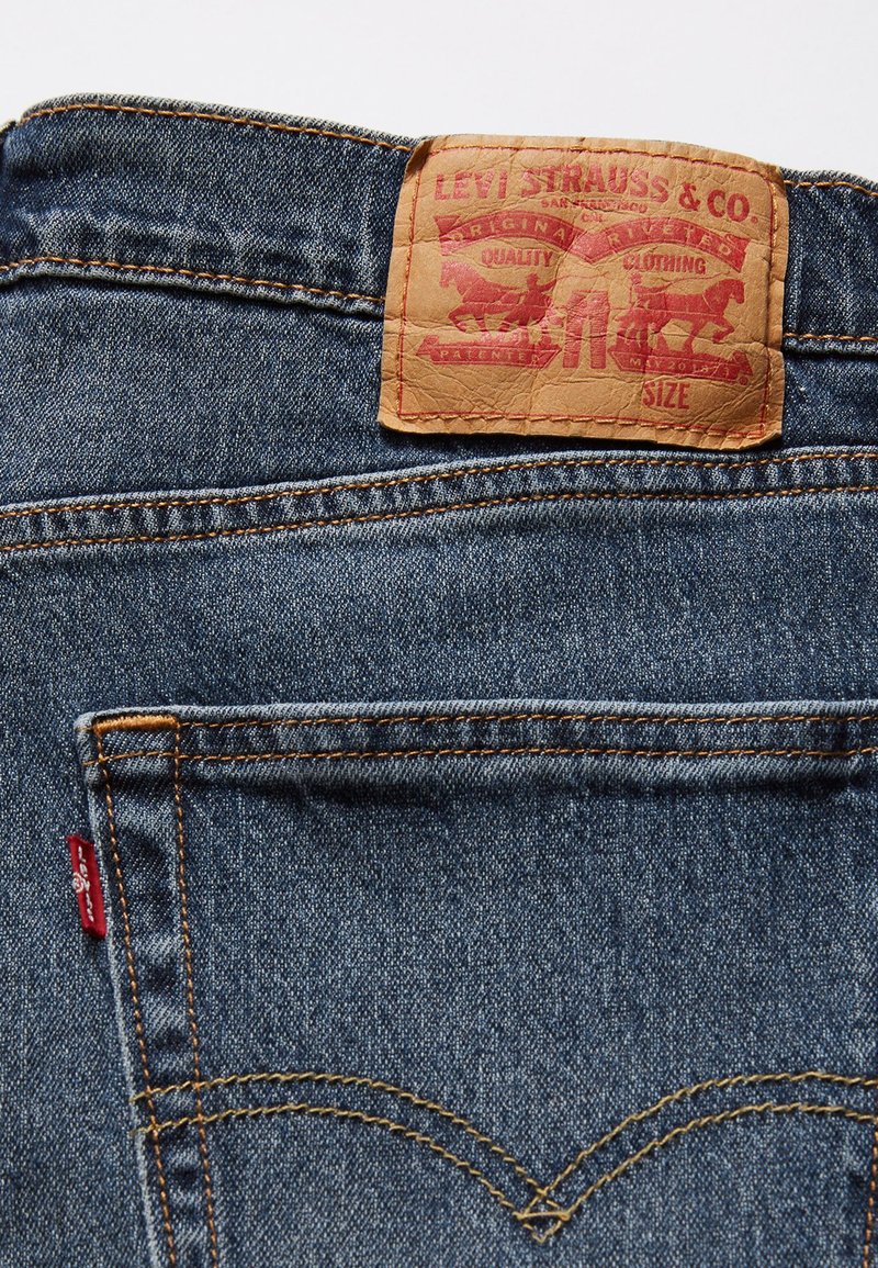 Levi's Jeans aus Denim mit einem braunen Lederetikett und rotem Grafikdesign. Blaues Gewebe mit goldenen Nähten und klassischen Taschendetails.