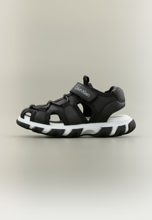 Black and white sporty open-toe sandal with Calvin Klein logo on adjustable strap and cushioned sole.