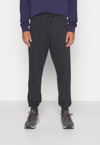 Mörkgrå joggers med elastisk midja och muddar, utrustad med dragsko och sidofickor. Matchat med grå sportskor.