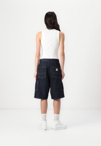 Denim cargo shorts i mörkblått med flera fickor, kontrastsömmar och avslappnad passform. Kombinerade med vita strumpor och sneakers.