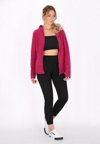 Fleece zip-up takki magentan värissä, jonka päällä on musta crop-top ja korkea vyötärö leggingsit. Jalkineet ovat valkoiset mustilla yksityiskohdilla.