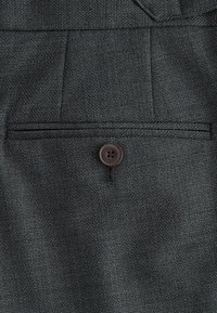 Tela tejida de color gris oscuro con una textura fina, que presenta un único bolsillo trasero asegurado con un botón redondo marrón.