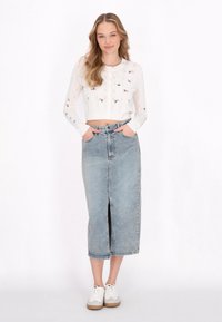 Pulover scurt tricotat alb cu broderie florală, asortat cu o fustă midi din denim albastru deschis, cu o fanta frontală. Tenisi albi casual.