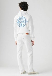 Witte capuchontrui met blauw "Paris" logo, gecombineerd met witte jeans. Kenmerken zijn onder andere een trekkoordcapuchon en geribde manchetten.