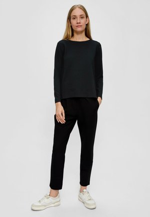 Zwarte lange mouwen top met een gestructureerd patroon, gecombineerd met zwarte tapered broek. Gemaakt met witte sneakers, wat een casual outfit presenteert.