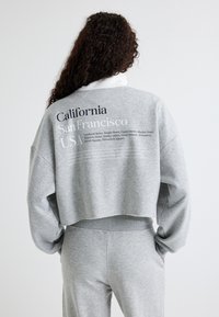 Grijze, korte sweatshirt met een ronde halslijn. Toont tekst: "California San Francisco USA" en straatnamen. Zacht, textuurstof, ontspannen pasvorm.