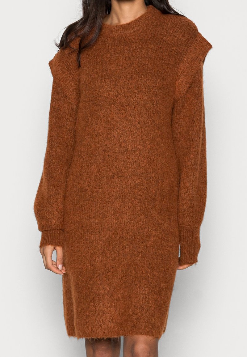 Robe-pull en maille marron surdimensionnée avec tissu texturé, encolure ronde et manches longues légèrement bouffantes. L'ourlet s'arrête juste au-dessus des genoux.