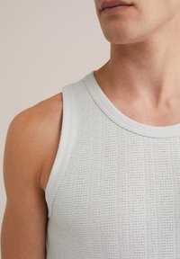 Lichtgrijze mouwloze tanktop, met een gestructureerde stof en een geribd patroon, en een ronde halslijn. Gladde schouders en armsgedeelte.