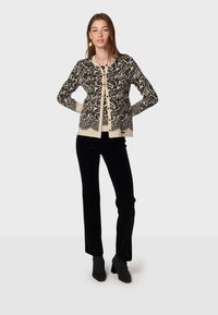 Svart och krämfärgad mönstrad cardigan med långa ärmar och knappar, kombinerad med svarta sammetbyxor och klackiga ankelskor.