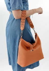 Borsa a tracolla in pelle beige con una forma morbida, caratterizzata da una tracolla intrecciata e dettagli in metallo argentato. Texture liscia e marchio discreto visibile.