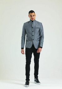 Grau, maßgeschneiderter Blazer mit hohem Kragen, schwarzen Knöpfen und Taschen vorne. Kombiniert mit schwarzen Slim-Fit-Hosen und metallischen Sneakers.