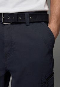 Marineblau Cargo-Shorts aus einem strukturierten Stoff; Ausstattung umfasst einen gewebten schwarzen Gürtel, Seitentaschen und detaillierte Nähte. Reißverschlusstasche am Bein.