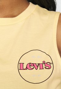 Gul ärmlös bomullsskjorta med en cirkulär grafik där "Levi's" står i fet rosa, och texten "EST 1873 SF/CA" i blå detaljer.
