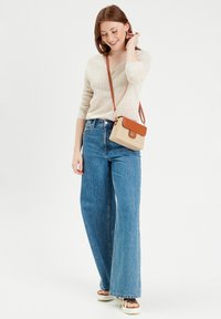 Pull en maille beige clair, jeans large taille haute bleu, et sandales compensées crème. Petit sac bandoulière tissé avec des accents bruns.