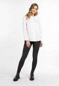 Weiße Bluse mit langen Ärmeln und rundem, gerafftem Kragen, vorn mit Knopfverschluss, kombiniert mit schwarzen, figurschmeichelnden Jeans und schwarzen Knöchelstiefeln.