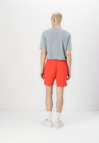 Maglietta in cotone grigia, vestibilità comoda, abbinata a pantaloni corti arancioni brillanti, cintura elastica, tessuto morbido e sneakers bianche. Sfondo semplice.
