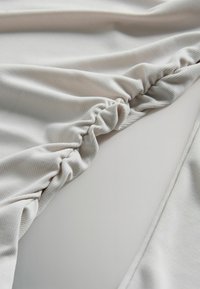 Jasnoszara, prążkowana tkanina z detalem zgromadzonego szwu, delikatnie drapowana, ukazująca gładką strukturę i subtelny połysk.