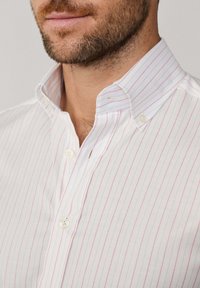 Biela košeľa s gombíkmi a úzkymi vertikálnymi ružovými pruhmi, s golierom a dvoma gombíkovými pätkami, vyrobená z hladkej bavlnenej tkaniny.