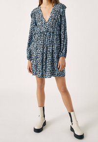 Kukallinen mekko syvällä V-aukolla, pitkät hihat ja röyhelöhihoilla. Sininen ja musta värimaailma, jossa pieniä kukkakuoseja. Yhdistettynä paksuihin valkoisiin nilkkabootseihin.