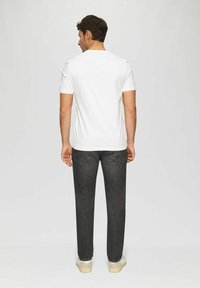 White short-sleeve t-shirt on a man, paired with dark gray jeans. The fabric appears smooth with a casual fit and standard crew neckline.