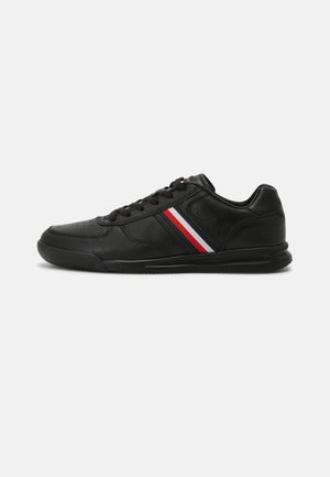 Czarny niski sneaker z wiązaniem na sznurówki, czerwono-biało-niebieskie paski boczne oraz teksturowana gumowa podeszwa na białym tle.