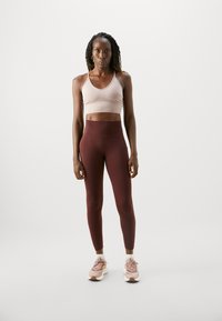 Top rosa chiaro a fascia corta, leggings alto vita bordeaux e scarpe sportive rosa. Texture del tessuto liscia e design aderente.