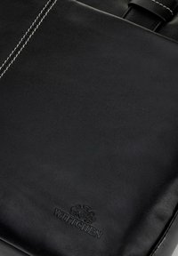 Schwarze Lederhandtasche mit sichtbar eingeprägtem Wittchen-Logo und kontrastierendem weißen Nähten in der oberen linken Ecke.