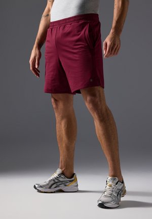 Bordeaux atletische shorts met een elastische tailleband en zijzakken, gecombineerd met grijs en zilver hardloopschoenen met gele accenten.