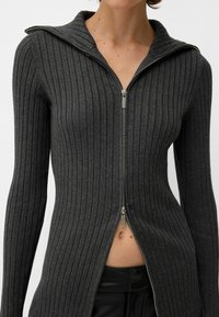 Grey ribbed long-sleeve zip-up top with a tall collar and front zipper, featuring a fitted design and vertical ribbing texture.