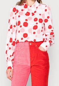 Blommig blus med röda och rosa blommor på en ljus bakgrund, matchad med corduroybyxor som är rosa på ena sidan och röda på den andra.