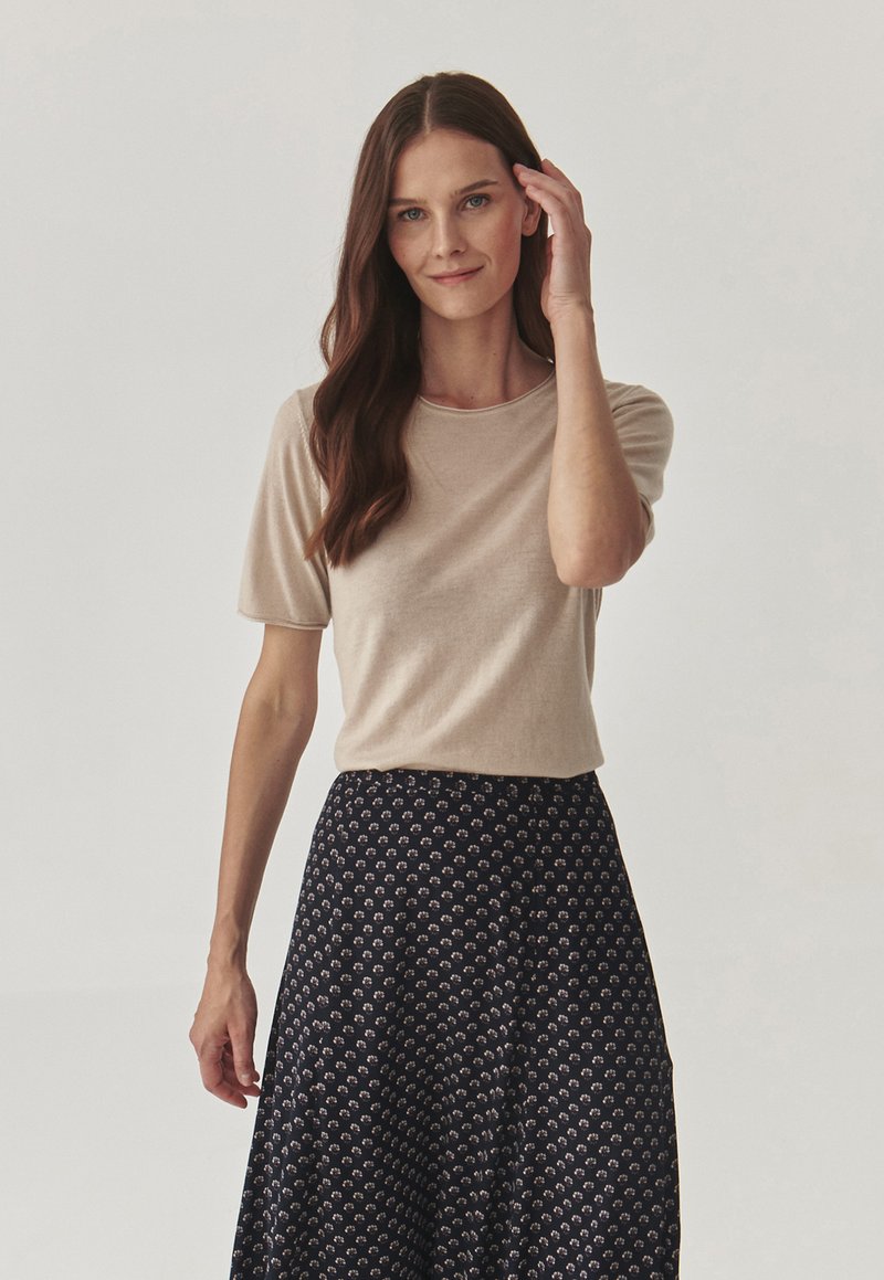Haut beige à manches courtes associé à une jupe bleu marine à motif floral, en tissu doux, coupe décontractée et encolure ronde.