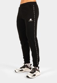 Zwarte joggers gemaakt van zachte stof met ribbeltextuur. Voorzien van een wit logo, een elastische tailleband en zijstripes met merktekst.