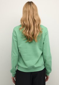 Sudadera verde menta hecha de tela suave, con un ajuste relajado, puños y cintura acanalados, mostrando la vista trasera sin ningún patrón.