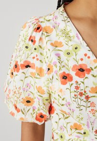 Rochie florală cu mâneci bufante, având modele de flori portocalii, roz și verzi pe un fundal alb. Material ușor, cu o textură moale.