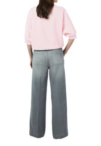 Rosa Sweatshirt mit Dreiviertelärmeln; kombiniert mit hoch taillierten, weit geschnittenen grauen Jeans mit zwei Gesäßtaschen.