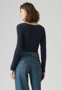 Marineblauwe geribbelde lange mouwen top met een gegolfde halslijn, gecombineerd met hoogwwaisted blauwe jeans met een leren patch en klassieke zakken.