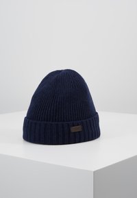 Knitted navy beanie with a ribbed design and a folded brim. Features a small, dark brown label on the front. Soft texture.