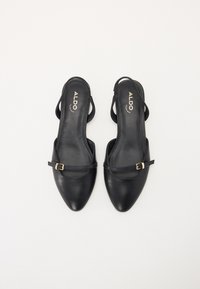 Chaussures slingback en cuir noir avec un bout pointu, une bride de cheville et un petit détail en boucle dorée. Texture lisse, design minimaliste.