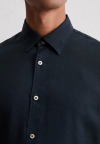 Marineblaues Hemd mit Spread-Kragen, hellen Knöpfen und einer glatten Textur, das eine taillierte Passform und ein minimalistisches Design betont.