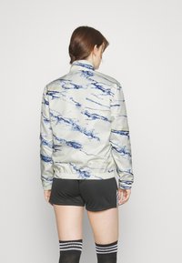 Lätt jacka med marmormönster i blått och grått; har hög krage, elastiska manschetter och midja för en åtsittande look.